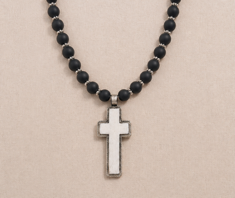 Mesa Noire Necklace with black onyx beads and carved bone cross pendant on linen background